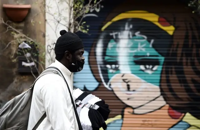 A street vendor, wearing a face mask walks in front of a mural in downtown Rome