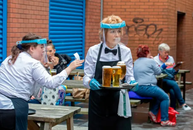 A waitress carrying beers while wearing a visor in a Belfast pub