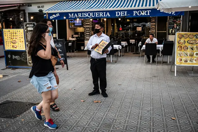 A worker wearing a protective face mask speaks to passing pedestrians outside a restaurant terrace on the Joan Borbo promenade in the Barceloneta neighborhood of Barcelona, Spain, on Tuesday, Aug. 18, 2020