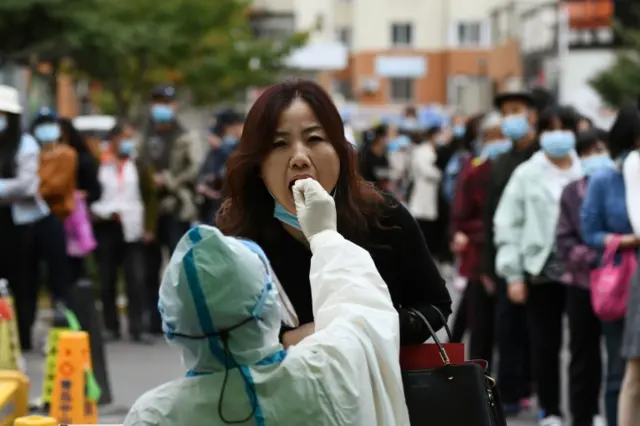 A medical worker in protective suit collects a swab from a woman for nucleic acid testing, following new cases of coronavirus in Qingdao, Shandong province, China, on 13 October 2020