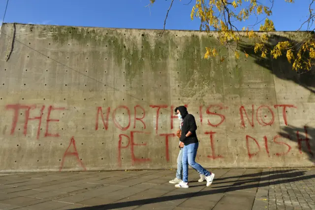 People walk past graffiti reading "the north is not a petri dish" in Manchester as the Government is preparing to impose stringent new coronavirus controls on 2.8 million people after talks with the local leaders for Greater Manchester failed to reach agreement.