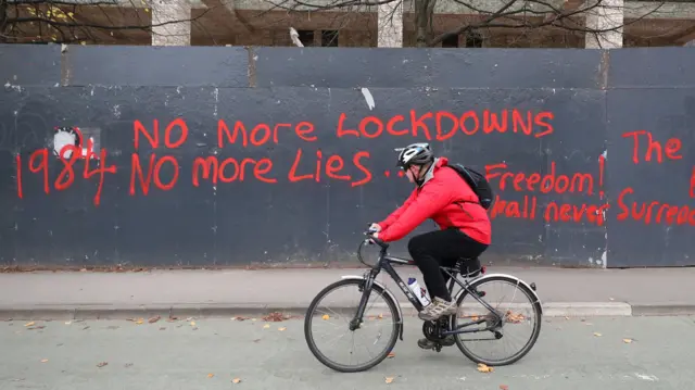 A man cycles past anti-lockdown graffiti in Manchester as the row over Greater Manchester"s coronavirus status continues