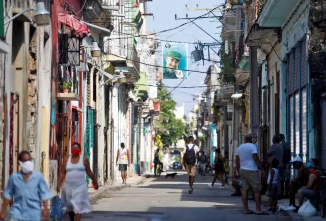 Several people walk down a street where a photo of Cuban leader Fidel Castro hangs on a street in Havana, Cuba