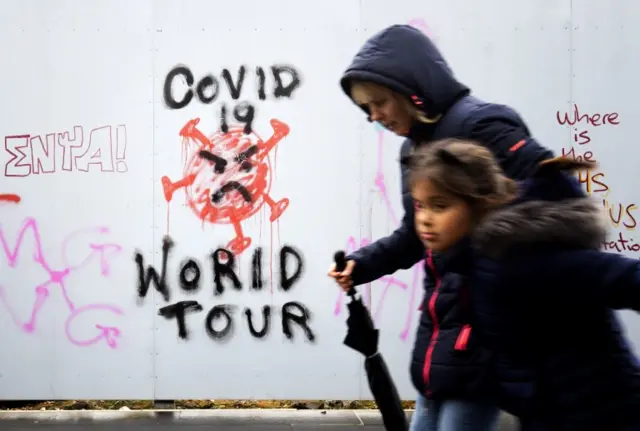 A woman and child walks past graffiti in Edinburgh saying 'Covid-19 World Tour'