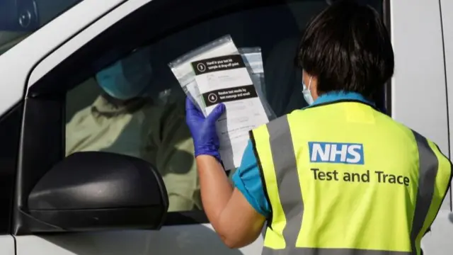 An NHS track and trace staff member holds up COVID-19 testing kits at a test centre