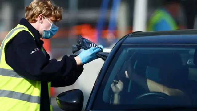 An NHS Track and Trace staff member collects samples at a drive-through test facility