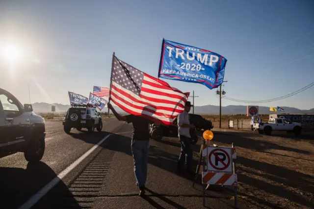 A woman waves a Trump and a US National flag as a caravan of cars from Kingman drives past supporting President Trump, as they gather for a presidential debate watch party, in Golden Valley, Arizona