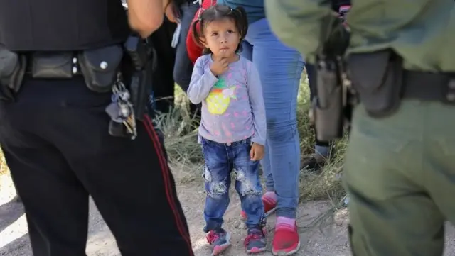 A Mission Police Dept officer (L) and a US Border Patrol agent watch over a group of Central American asylum seekers before taking them into custody in Texas