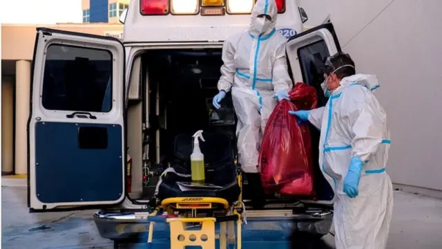 Workers wearing protective equipment clean an ambulance in the US