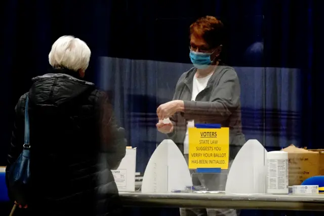 A poll worker assists a voter from behind a plastic barrier at an early voting site inside the Bismarck Event Center as the coronavirus outbreak continues in Bismarck, North Dakota.