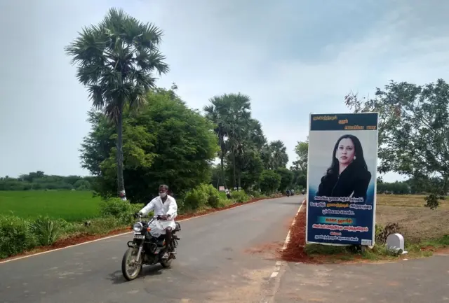 A man drives past a banner of US Democratic vice presidential nominee Kamala Harris at the entrance to the village of Thulasendrapuram, India