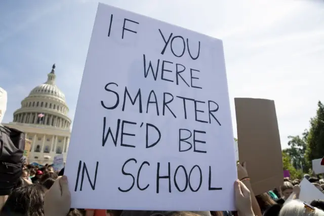 A protester holds a placard reading 'if you were smarter we'd be in school'