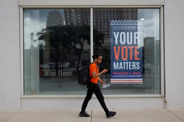 A pedestrian passes a sign urging people to vote outside the site of the Democratic National Convention (DNC), which will be a largely virtual event due to the coronavirus disease (COVID-19) outbreak, in Milwaukee, Wisconsin, U.S., August 17, 2020