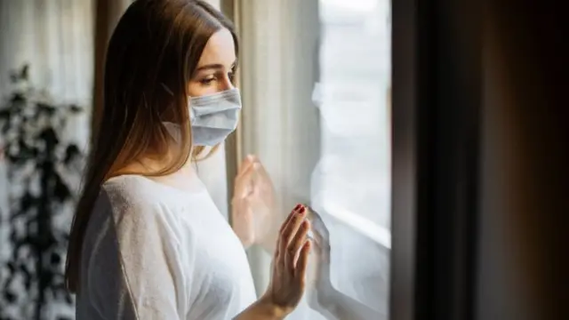 masked woman looking out of window