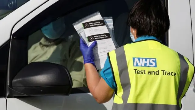 An NHS track and trace staff member holds up COVID-19 testing kits