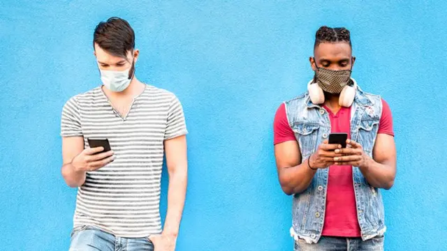 Two men wearing face coverings look at their phones