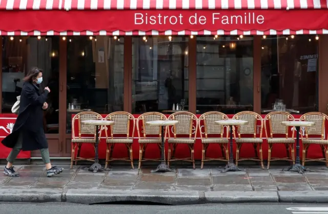 A masked woman walks past a restaurant in Paris