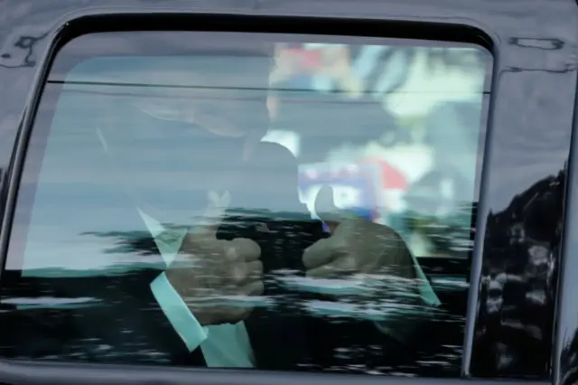 President Donald Trump gestures from a car as he rides in front of the Walter Reed National Military Medical Center