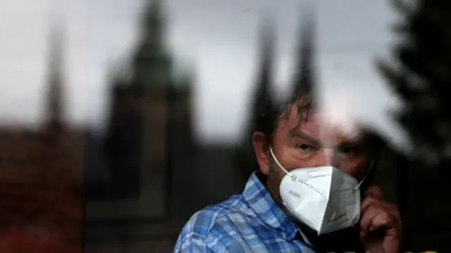 A man wearing a face mask looks out of a window of a cafe in Prague