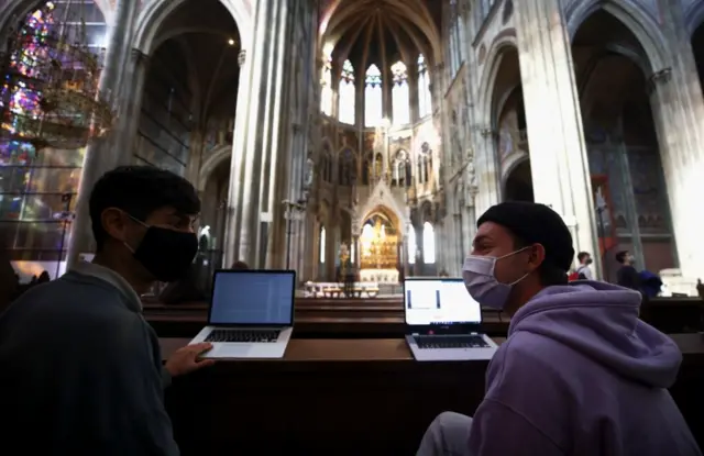 Masked students talk while working at their laptops in Vienna's Votivkirche