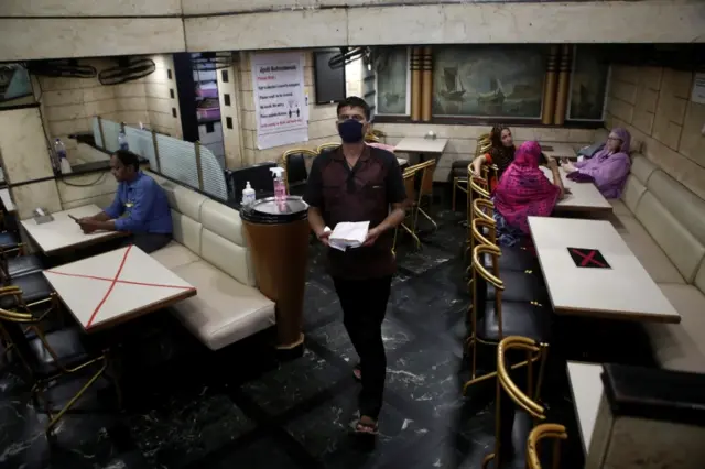 A waiter walks past tables that have been blocked to maintain social distancing at restaurant