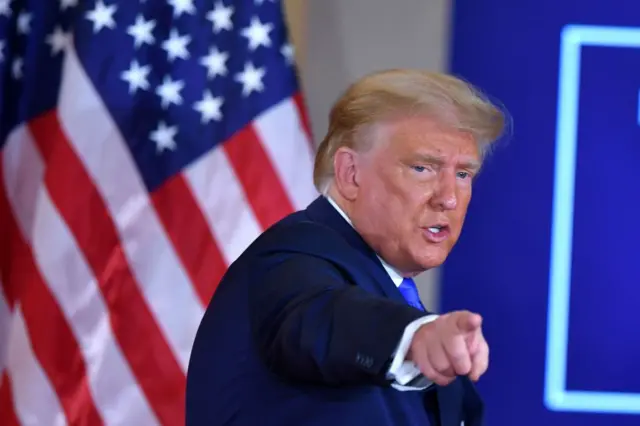 President Trump points with the US flag behind him