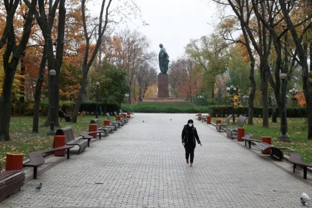 A woman wearing a face mask walks in a park in Ukraine