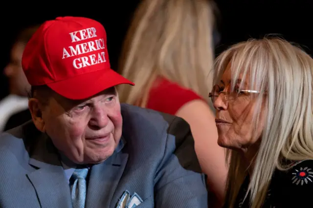 Sheldon Adelson wears a cap reading: Keep America Great