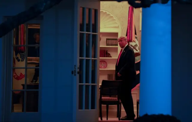 Donald Trump stands inside the White House after leaving the briefing