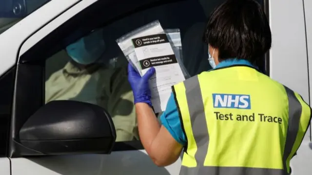 An NHS track and trace staff member holds up COVID-19 testing kits