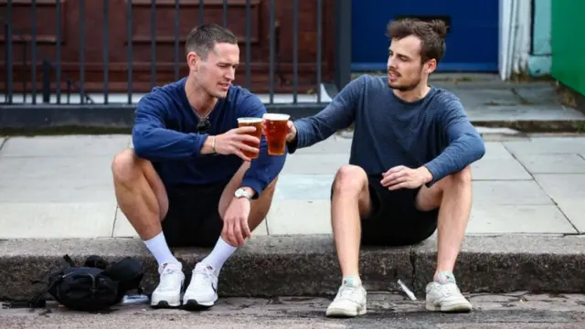 Two men holding beers in takeaway cups