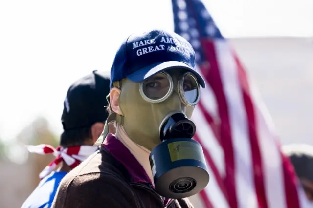 A supporter of Donald Trump wears a "Make America Great Again" hat and a gas mask