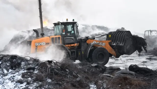 Digger moving smouldering tyres