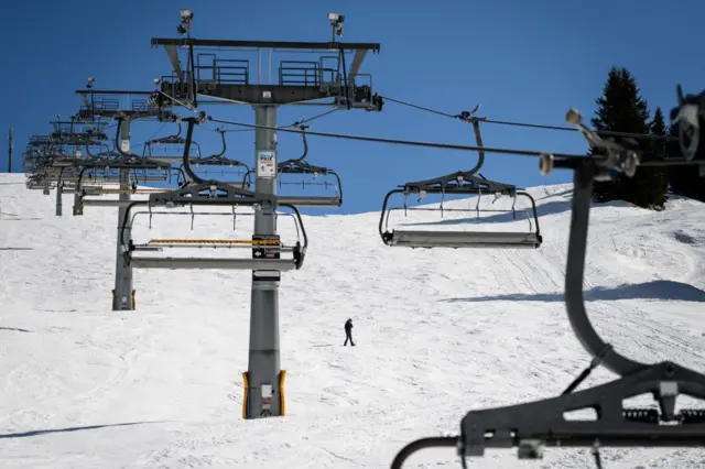 A man walks across a ski slope under a closed ski lift