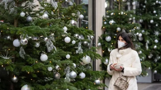 Woman wearing a face covering while walking past Christmas trees