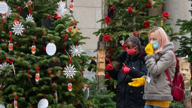 People walk past Christmas trees wearing masks