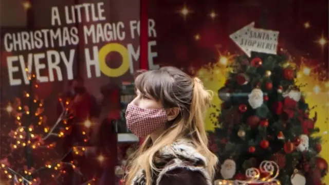 Woman wearing a mask and walking past a Christmas shop display