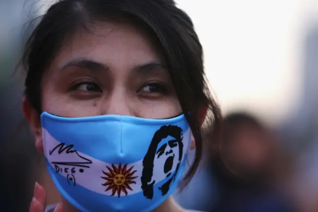 A fan wearing a face mask with a logo of Argentine soccer great Diego Maradona gathers to mourn his death, at the Obelisk of Buenos Aires, Argentina November 25, 2020.