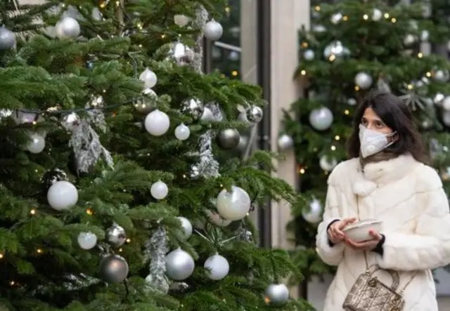 Woman in mask next to Christmas tree