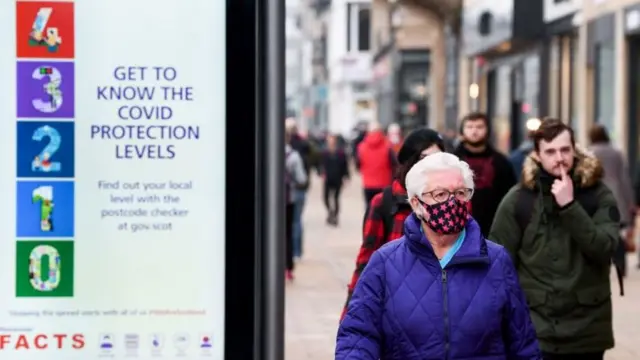 A woman wearing a mask walks past a Covid sign in Scotland