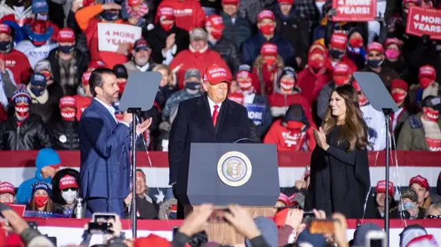 US President Donald Trump (C) speaks as Kimberly Guilfoyle (R) and Donald Trump Jr. (L) listen during a campaign held at the Kenosha Regional Airport in Kenosha, Wisconsin, United States on November 02, 2020