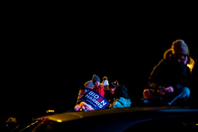 Girls sit on top of a car during an election eve rally with Kamala Harris