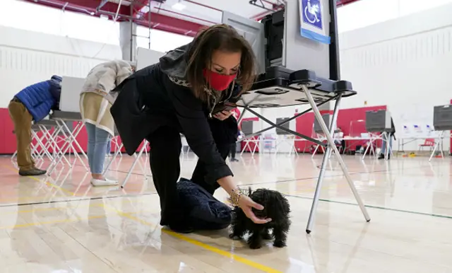 A voter stops her dog from barking as she fills in her ballot at Greenwich High School in Greenwich, Connecticut