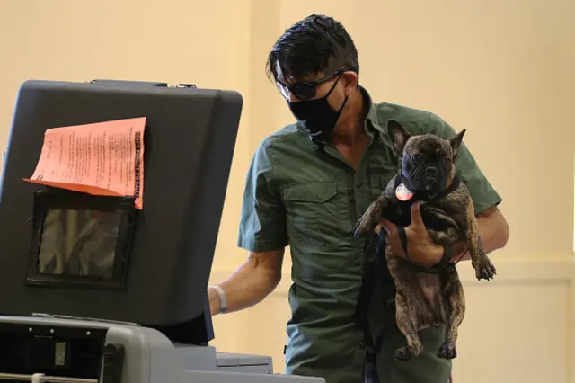 A man wearing a face mask holds his dog in one hand while casting his vote with the other in Miami, Florida