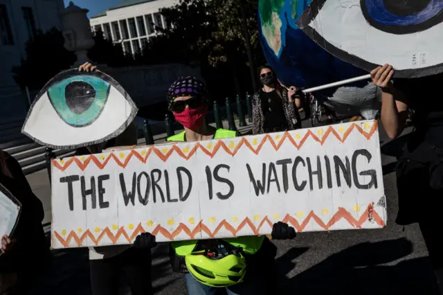 Climate protester in Washington DC with a sign reading 'the world is watching'