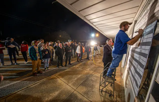 Cairo Messenger newspaper publisher and editor Randy Fine, center, calls out election results as Steve Reagan writes them on the board on the front wall of the newspaper for the voters gathered in the street on November 3, 2020 in Cairo, Georgia