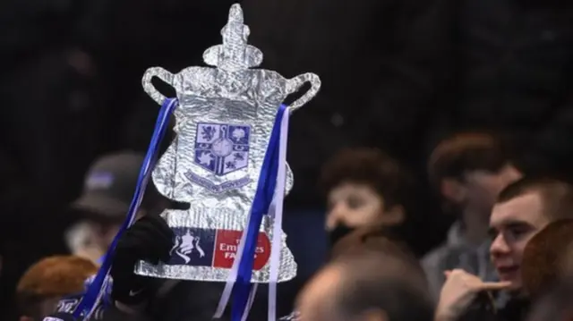 A fan holds up a foil FA Cup