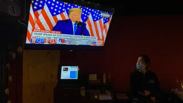 A restaurant worker wearing a protective face mask watches US President Donald Trump"s speech on a TV during US presidential elections, at a restaurant in Beijing, China, 04 November 2020.