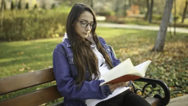 A woman reading a book on a bench
