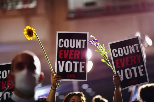 Activists hold up flowers and signs stating "COUNT EVERY VOTE" across the street from where votes are still being counted, two days after the 2020 U.S. presidential election, in Philadelphia, Pennsylvania,